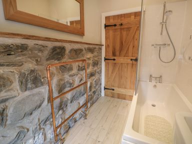 A bathroom with a bathtub shower combination copper towel rail stone wall wooden door and wooden framed mirror at Tyn Ffynnon in Dyffryn Ardudwy