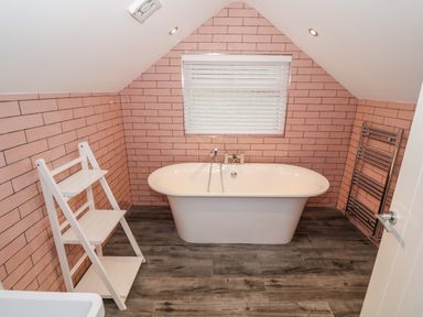 A bathroom with a freestanding bathtub white shelves wood floor and pink tiled walls at Argraig in Llanbedrog