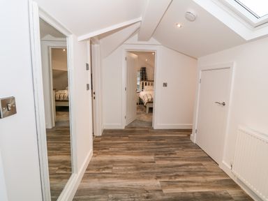 A hallway with wood flooring a mirror on the wall a radiator and a door leading to a bedroom at Argraig Llanbedrog