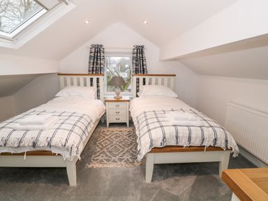 A bedroom with two single beds nightstand lamp window with curtains and skylight at Argraig in Llanbedrog