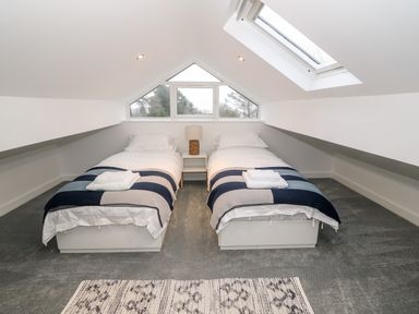 A bedroom with two single beds with striped blankets and a bedside table with a lamp at Argraig in Llanbedrog