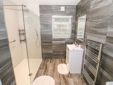 A bathroom with a walk in shower a white sink unit a mirror a window with blinds and a heated towel rail at Argraig in Llanbedrog