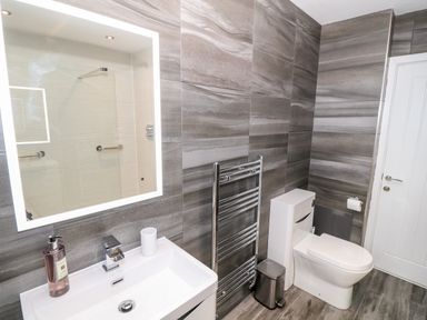 A bathroom with a sink vanity a large mirror toilet towel rack and a trash bin at Argraig in Llanbedrog