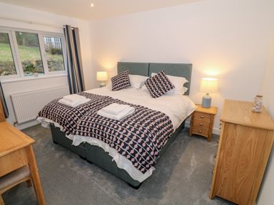 A bedroom with a double bed bedside tables lamps a dresser and a desk with chair at Argraig in Llanbedrog