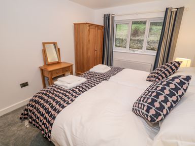 A bedroom with a double bed, patterned pillows and bed runner, a wooden wardrobe, dressing table with mirror, and window with curtains at Argraig in Llanbedrog