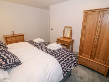 A bedroom with a bed with patterned pillows and blanket alongside a wooden wardrobe and dressing table at Argraig in Llanbedrog