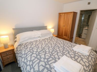 A bedroom with a double bed bedside tables with lamps a wooden wardrobe and an open door to a bathroom at Argraig in Llanbedrog