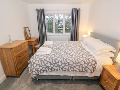 A bedroom with a double bed a wooden dresser a wooden desk with a mirror and a window with curtains at Argraig in Llanbedrog