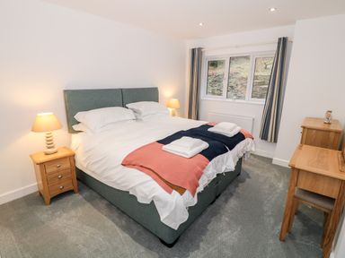 A bedroom with a double bed bedside tables lamps a desk and window with curtains at Argraig Llanbedrog