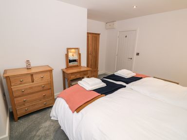 A bedroom with two beds white bedding wooden dresser and vanity unit at Argraig Llanbedrog