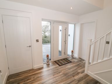 An entrance hallway with a white front door flanked by sidelights two doors a staircase and a wooden floor at Argraig in Llanbedrog