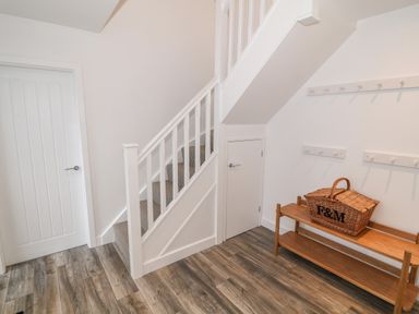 A hallway with wooden flooring a white staircase a wooden bench with a wicker basket and white walls with hooks at Argraig in Llanbedrog