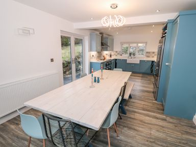 A kitchen with blue cabinets a wooden dining table with chairs and candles at Argraig in Llanbedrog