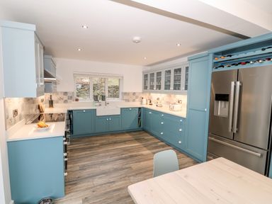 A kitchen with blue cabinets a wooden floor and a stainless steel refrigerator at Argraig in Llanbedrog