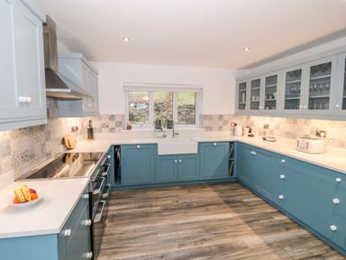 A kitchen with blue lower cabinets and light blue upper cabinets with glass doors a white countertop and patterned tile backsplash at Argraig in Llanbedrog