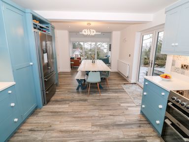 A kitchen with blue cabinets a stainless steel refrigerator and oven a wooden dining table with chairs and bench seating at Argraig in Llanbedrog