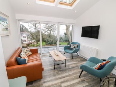 A sitting room with a brown sofa two blue chairs a coffee table and a wall mounted tv at Argraig in Llanbedrog