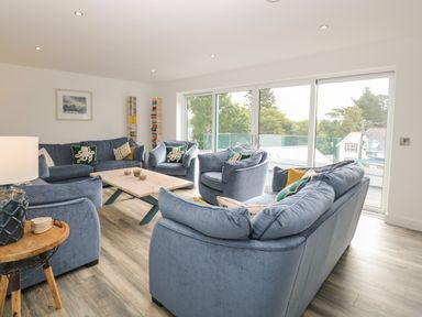 A living room with blue sofas and armchairs around a wooden coffee table next to large sliding glass doors at Argraig in Llanbedrog