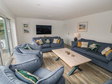 A living room with blue sofas, a wooden coffee table, a wall-mounted TV, and framed pictures at Argraig in Llanbedrog