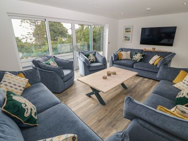 A living room with blue sofas and armchairs around a wooden coffee table and a wall-mounted television at Argraig in Llanbedrog