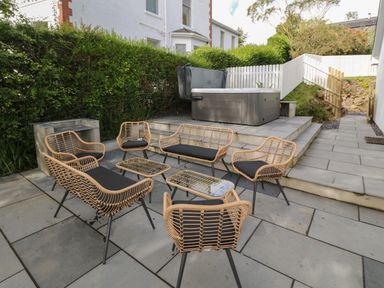 An outdoor patio area with wicker chairs and tables and a hot tub in a garden at Argraig in Llanbedrog