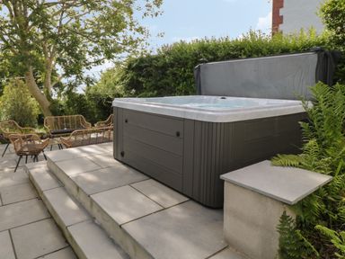 An outdoor patio with a hot tub on a raised platform and wicker chairs around a table at Argraig in Llanbedrog