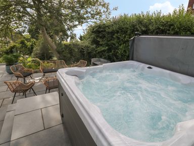 An outdoor patio area with a hot tub and seating with chairs and a bench surrounded by greenery at Argraig in Llanbedrog