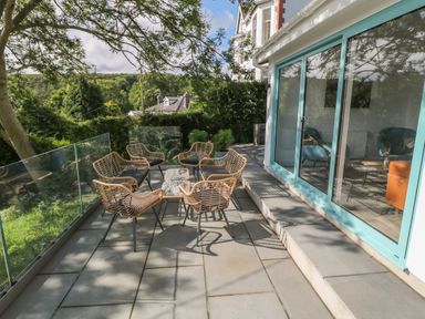 An outdoor patio with wicker chairs and small tables next to a building with large sliding glass doors at Argraig in Llanbedrog