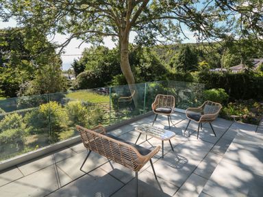 An outdoor patio with woven chairs and a small table surrounded by glass panels and greenery at Argraig in Llanbedrog