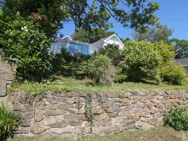 A house on a hill with a stone retaining wall and various bushes and trees at Argraig in Llanbedrog