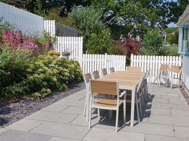 An outdoor patio with a long dining table and chairs next to a white picket fence and garden at Argraig in Llanbedrog
