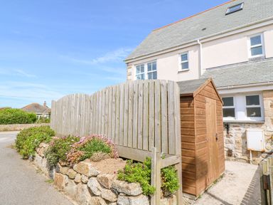 A wooden shed near a stone wall with plants and a wooden fence beside a house at Henrys Croft in Lizard