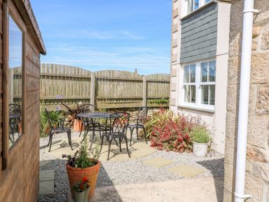 An outdoor patio area with metal chairs and table surrounded by potted plants and a wooden fence at Henrys Croft in Lizard