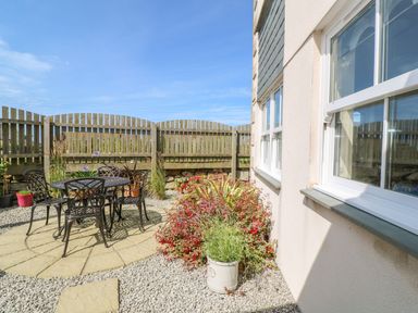 An outdoor patio with a round metal table and four chairs surrounded by plants and a wooden fence at Henrys Croft in Lizard