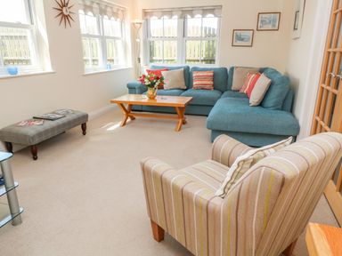 A living room with a blue corner sofa, a wooden coffee table, an upholstered armchair, a bench, and windows at Henrys Croft in Lizard