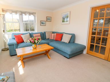 A living room with a blue sectional sofa red and beige cushions a wooden coffee table with flowers and paintings on the wall at Henrys Croft in Lizard
