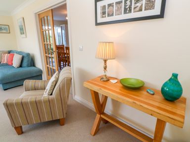 A living room with a wooden console table holding a lamp plate and vase next to an armchair and sofa at Henrys Croft in Lizard