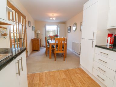 A kitchen with white cabinets and a wooden dining table with chairs at Henrys Croft in Lizard