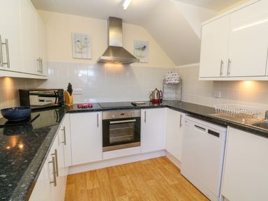 A kitchen with white cabinets black countertops a built-in oven a dishwasher a toaster a kettle and wooden floor at Henrys Croft in Lizard
