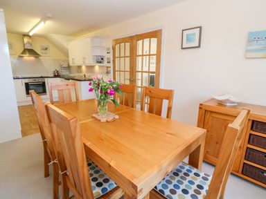 A dining room with a wooden table and chairs with polka dot cushions and a kitchen in the background at Henrys Croft in Lizard