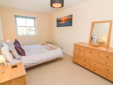 A bedroom with a bed nightstand chair dresser with mirror and wall art at Henrys Croft in Lizard
