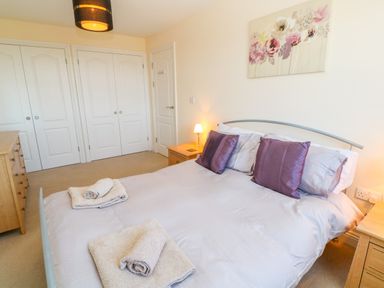 A bedroom with a bed with purple pillows and folded towels on it a wooden dresser and bedside tables with lamps at Henrys Croft in Lizard