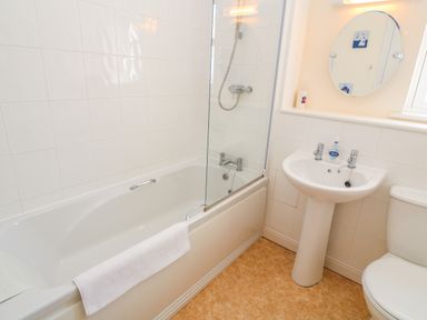 A bathroom with a bathtub shower combination towel on the tub a pedestal sink with soap and a round mirror above and a toilet at Henrys Croft in Lizard