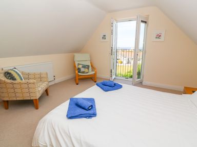 A bedroom with a white bed and blue towels two chairs and an open balcony door at Henrys Croft in Lizard