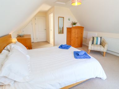 A bedroom with a double bed white linens blue towels wooden furniture and an armchair at Henrys Croft in Lizard
