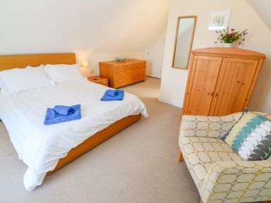 A bedroom with a double bed with white bedding and blue towels a wooden dresser a wardrobe a patterned armchair and a wall mirror at Henrys Croft in Lizard