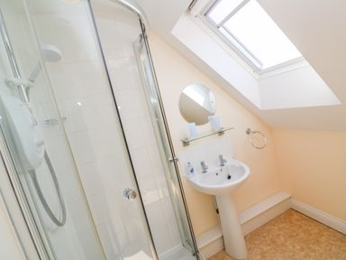 A bathroom with a glass shower enclosure a white sink a round mirror and a skylight at Henrys Croft in Lizard