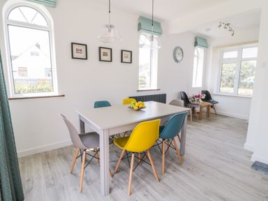 A dining room with a table surrounded by colorful chairs and windows at Senafe in Widemouth Bay