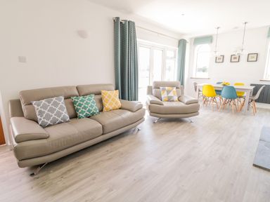 A living room with a beige sofa and armchair with patterned cushions and a dining table with colorful chairs at Senafe in Widemouth Bay