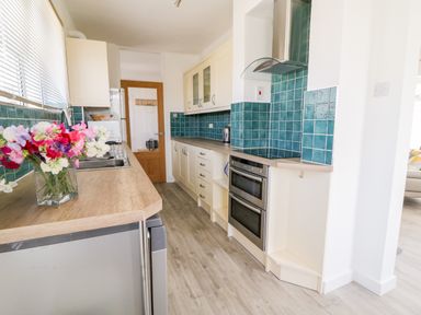 A kitchen with wooden countertops blue tiled backsplash stainless steel oven and a vase of flowers at Senafe in Widemouth Bay